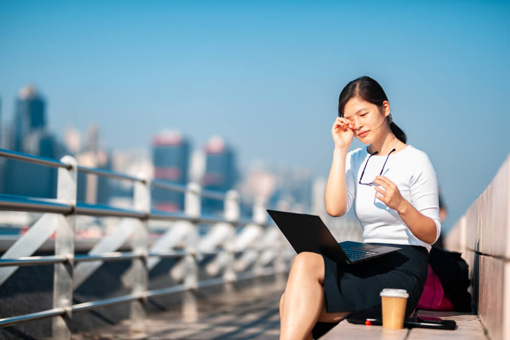 Young woman with dry eyes sitting outside with laptop