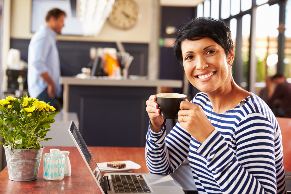 woman drinking coffee in coffee shop with laptop